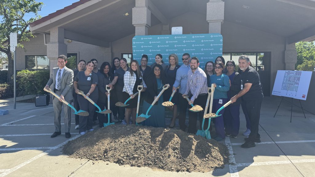 Numerous event attendees shovel ceremonial dirt with teal shovels at Rural Health Clinic 2 groundbreaking in Los Banos