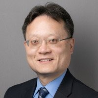 Headshot of a male doctor with glasses, smiling wearing a tie and a blue shirt