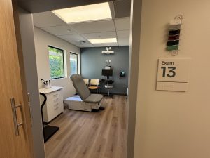 A patient exam room inside a care center with medical equipment and two windows facing a courtyard