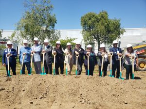 Group of men and women in hardhats and shovels standing alongside each other on a mound of dirt