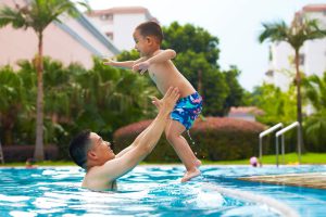 Little boy jumps into his father's arms while in the pool.