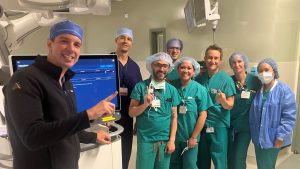 A group of medical staff in scrubs and surgical caps posing around equipment inside a hospital
