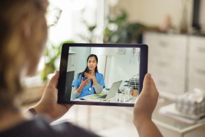 A woman holding a tablet consults with a medical professional on the screen