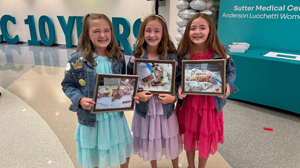 Triplets holding photos when they were born.