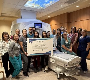 Group of medical professionals and administrators gather around a new MRI machine holding a sign marking the machine's arrival