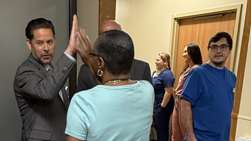 Healthcare staff and administrators visiting in hallways with a man and a woman high-fiving each other in the left foreground