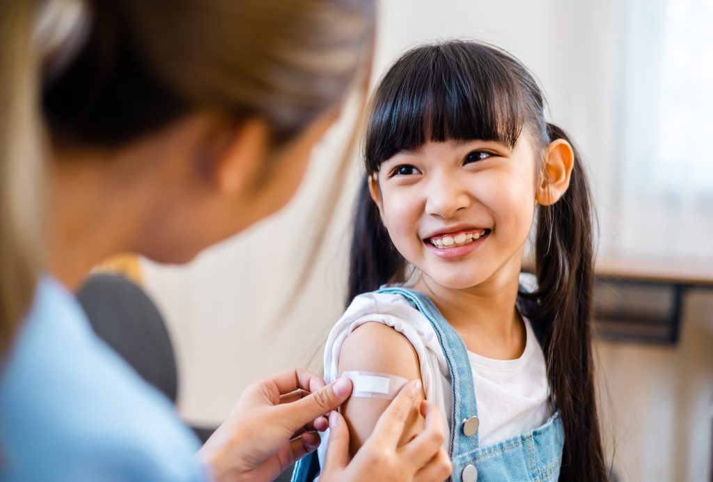Childhood vaccination. Asian young woman doctor vaccinating little girl at home. Vaccine for covid-19 coronavirus, flu, infectious diseases.