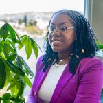 Photo of woman with glasses, braids, and magenta jacket.