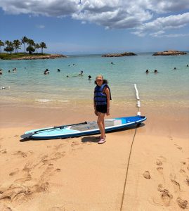 A teenage girl stands next to a paddleboard at the beach