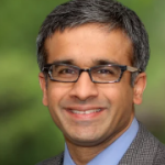 Male doctor headshot, smiling in a suit
