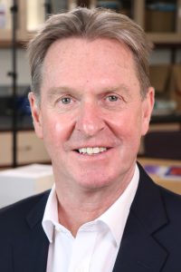 Headshot of David Kerr, Caucasian male with blond hair wearing a black blazer over a white button-down shirt