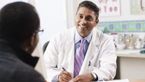 Doctor smiling and taking notes while talking with patient.
