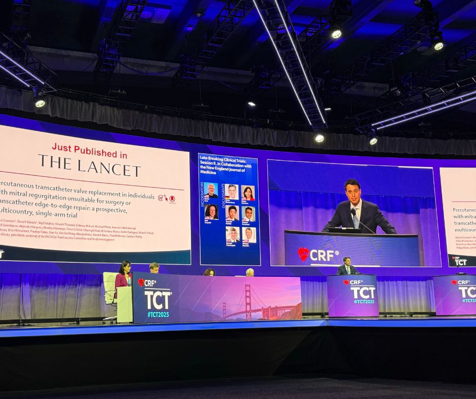 Picture of a conference, purple lighting, the lancet featured on one screen, the doctor presenter on the other.
