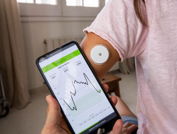Smart phone showing glucose levels, person's arm in foreground