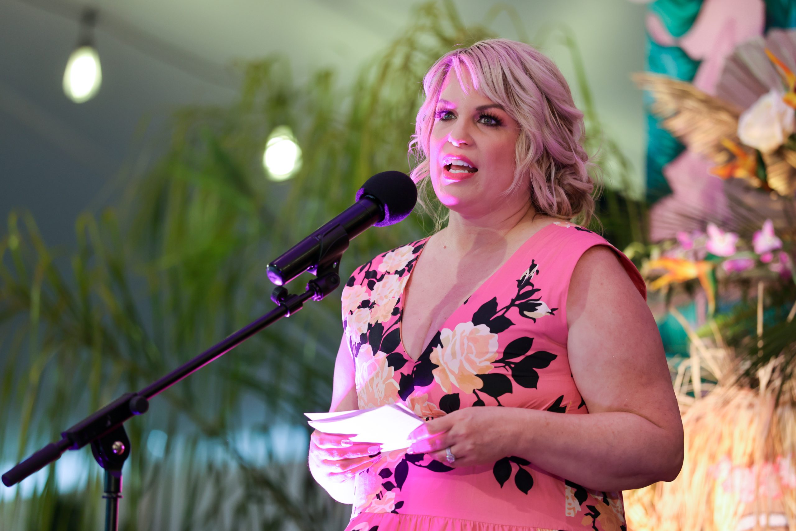 A woman in a pink dress speaks in front of a microphone