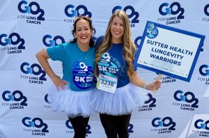 Two women posing in tutus in front of a GO2 for Lung Cancer step and repeat.