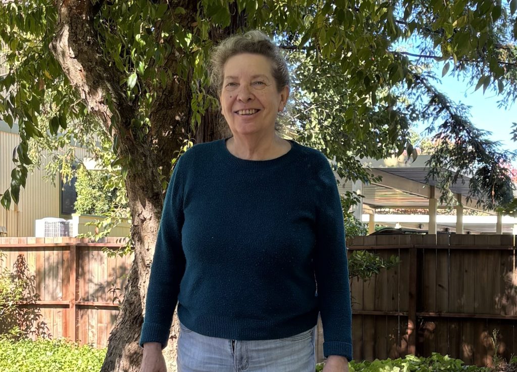 Photo of a senior woman wearing a blue sweater in a garden