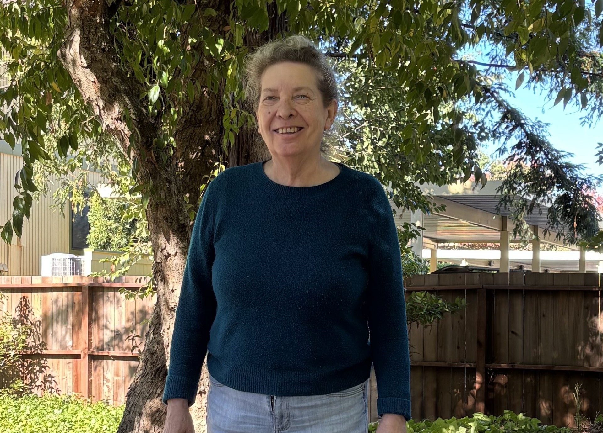 Photo of a senior woman wearing a blue sweater in a garden