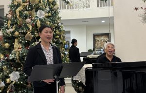 Image of a woman singing and man at the piano with christmas tree behind them