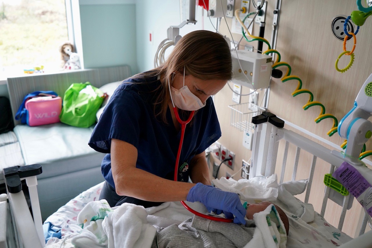 Doctor in a masks checks vitals on a baby in the NICU
