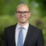 photo of a man, with buzzed hair, glasses and a suit