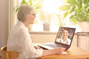 Senior caucasian woman sitting at desk with laptop during virtual visit with physician