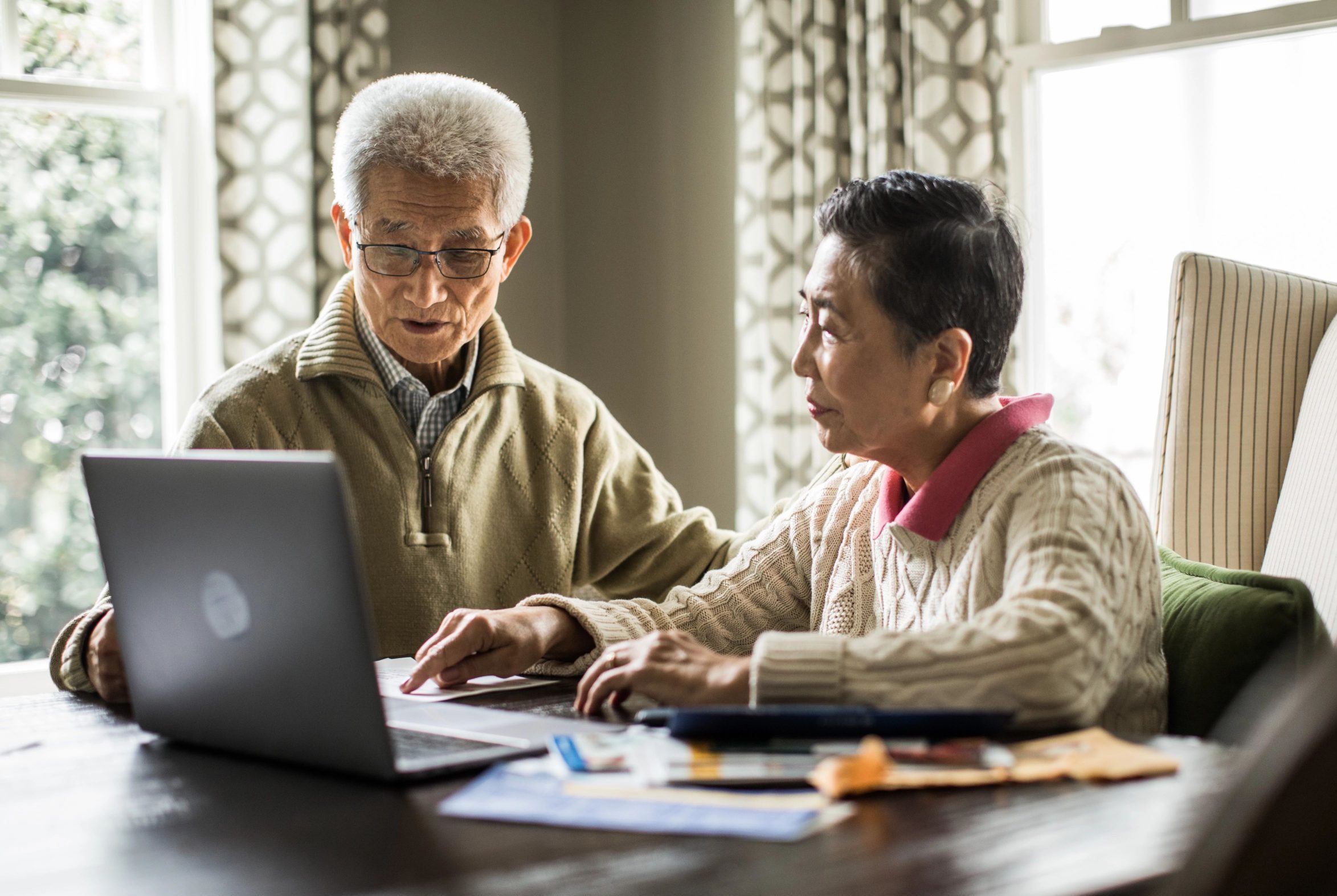 Asian couple at table looking together at laptop screen.