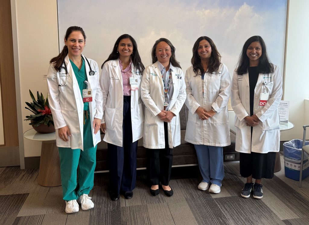 Five female cardiologists stand in their white coats