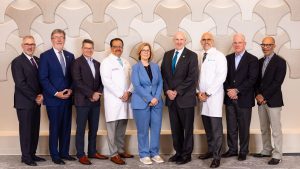 A group of professional executives in a combination of suits and white lab coats posing in front of a textured wall.