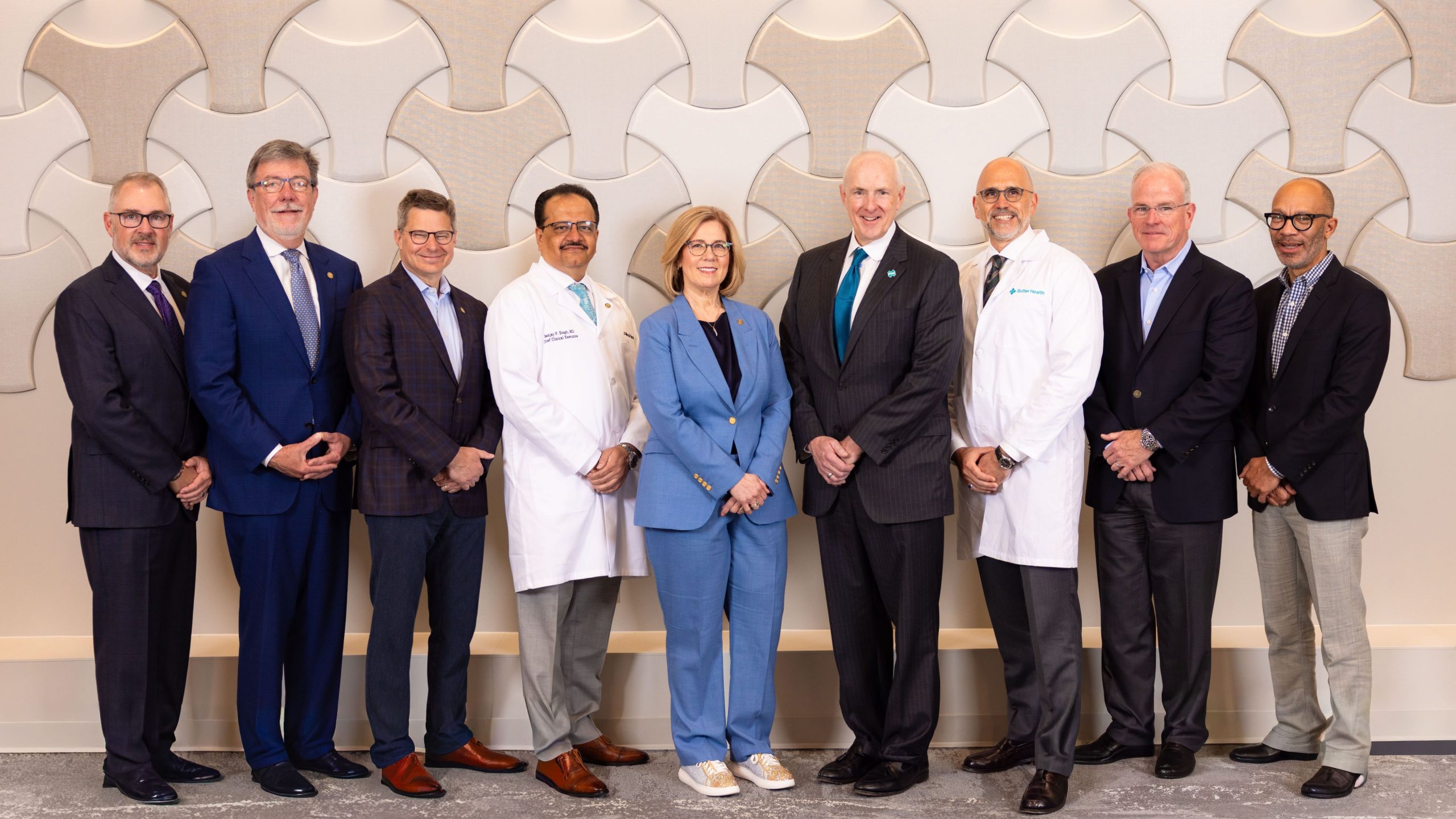 A group of professional executives in a combination of suits and white lab coats posing in front of a textured wall.