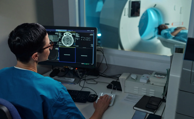 Radiologist watches from room as patient moves through an MRI machine