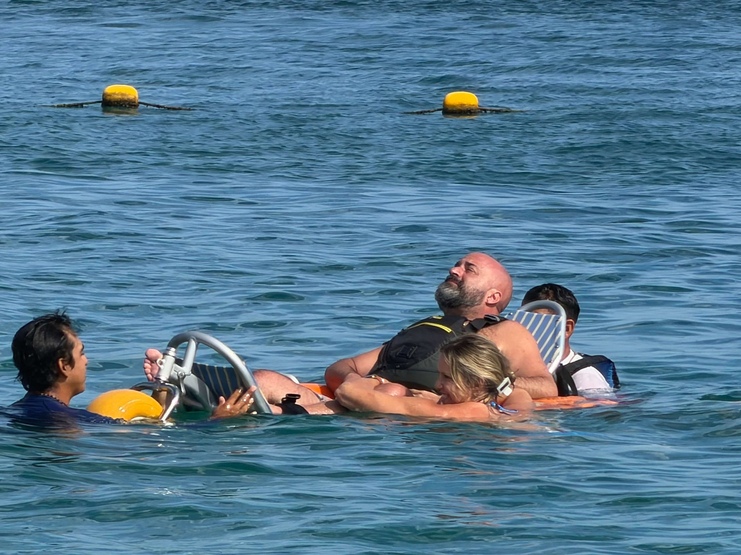 A man floats in ocean waters with assistance
