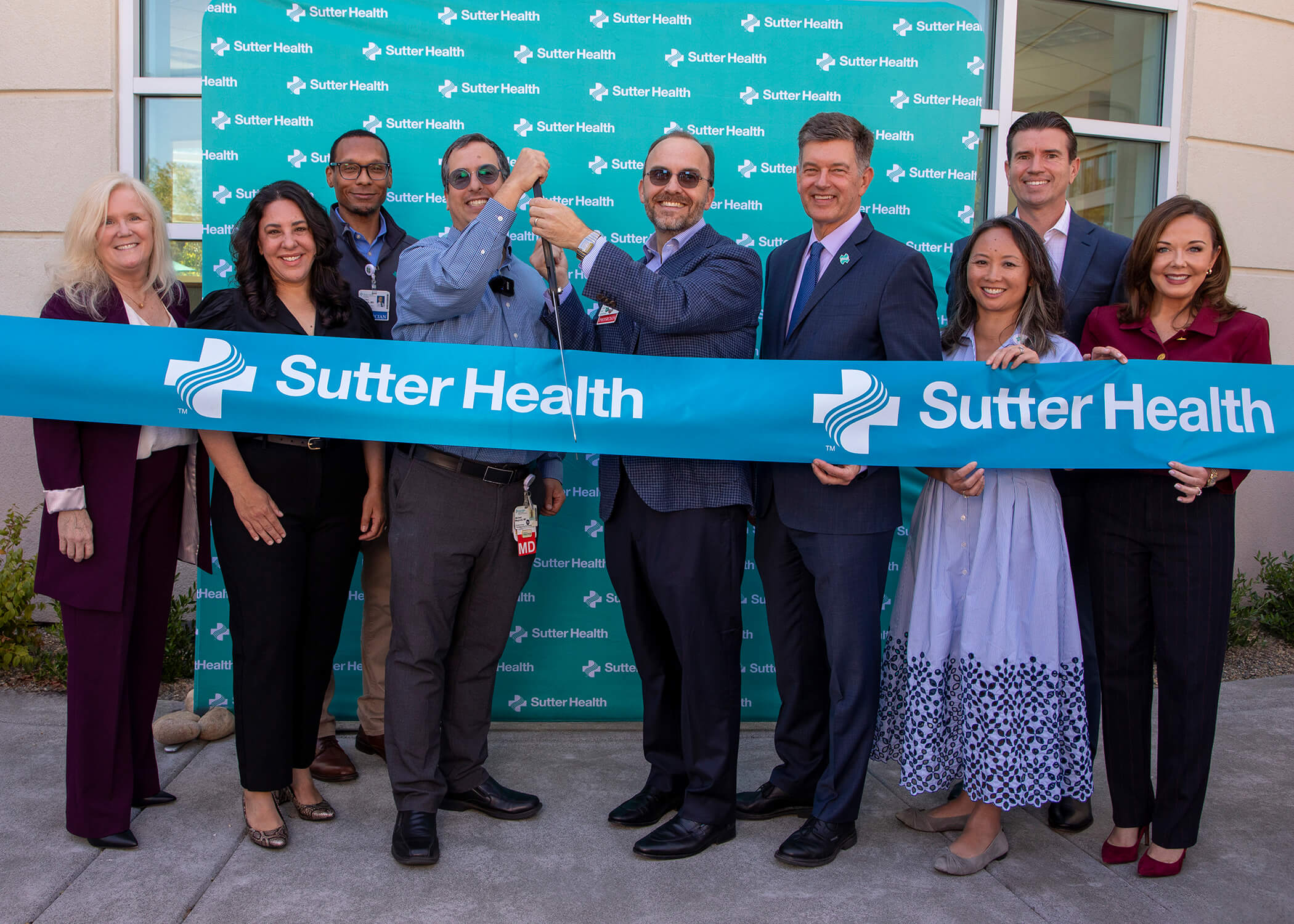 A group of people hold a Sutter Health banner at a ribbon cutting ceremony