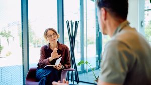 Female professional giving guidance and support to a man during a therapy session in a modern office setup