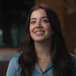 Female doctor, with brown hair, wearing teal shirt and gold necklace smiling
