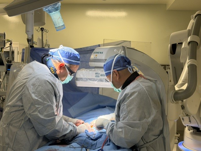 Two surgeons in surgical caps and gowns perform a procedure together.