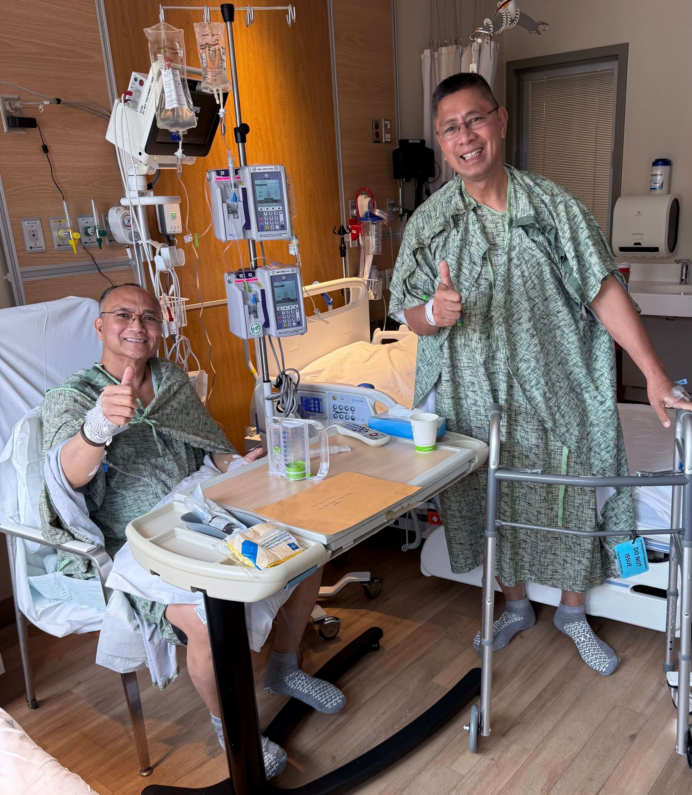 Two Filipino priests in hospital gowns posing with thumbs up