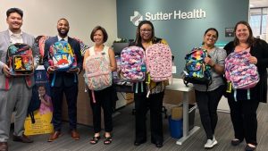 A group of professional men and women standing in a lobby holding backpacks 