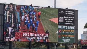 A scoreboard with an image of children walking across a baseball field