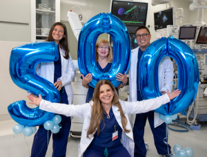 A group of medical professionals in an operating room with blue balloons that say 5-0-0