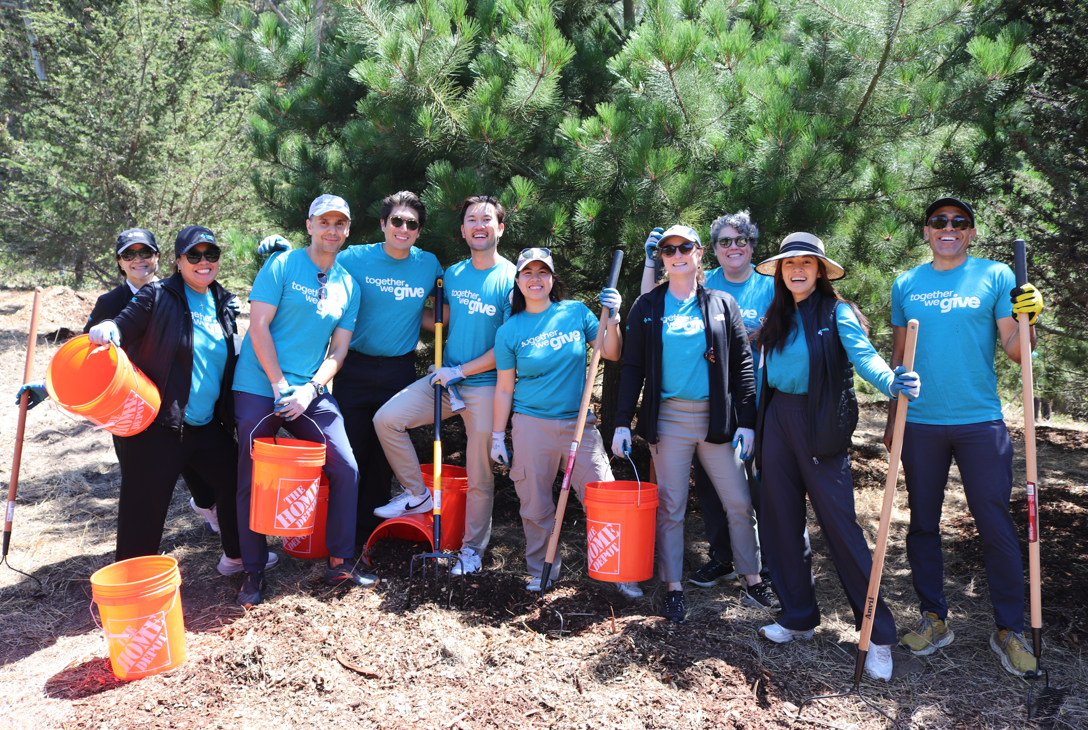 A group of volunteers with teal shirts, rakes and buckets