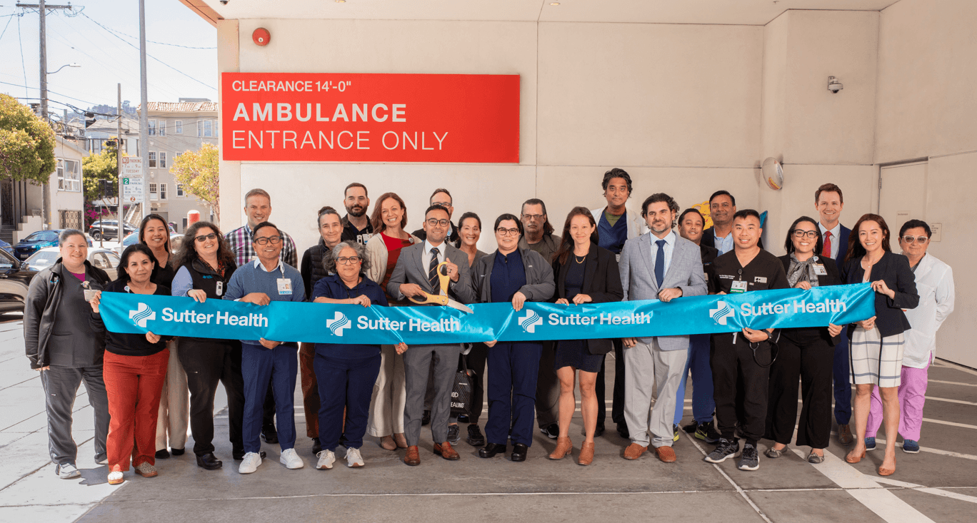 A large group of people in an ambulance bay cut a Sutter Health ribbon
