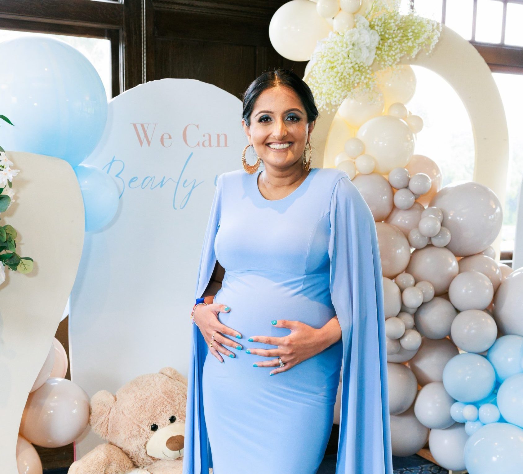 Nisha Patel at her baby shower A woman holds her baby bump in front of balloons at a baby shower