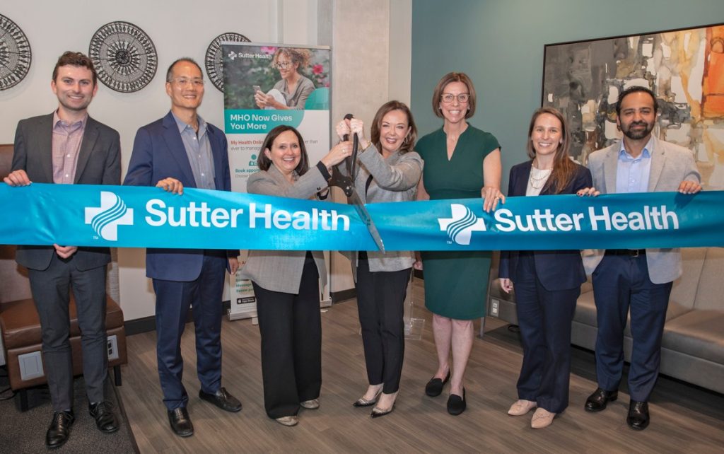 people stand behind a Sutter Health ribbon with large scissors