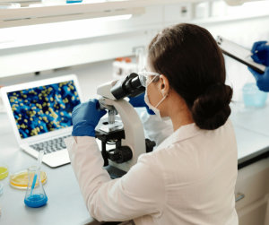 woman with dark hair looking into microscope wearing lab coat