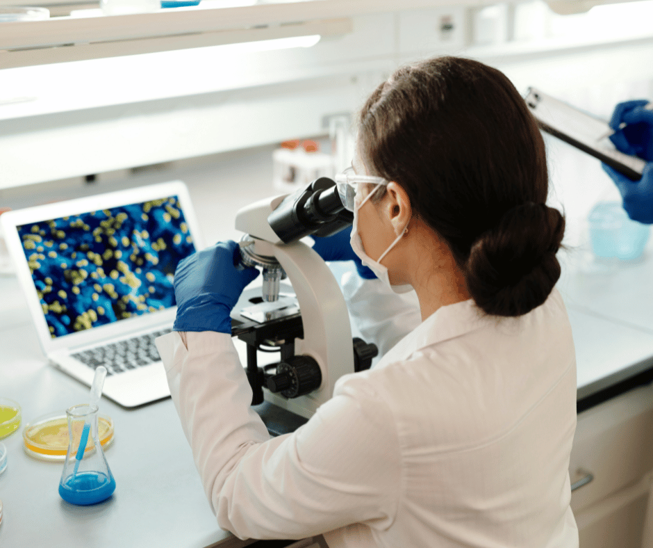 woman with dark hair looking into microscope wearing lab coat