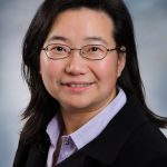 Smiling female researcher with collar shirt on, glasses and black sweater
