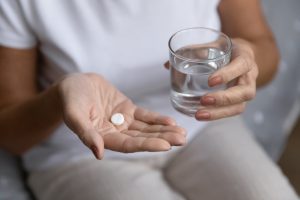 Picture of a person holding a glass of water and some pills.
